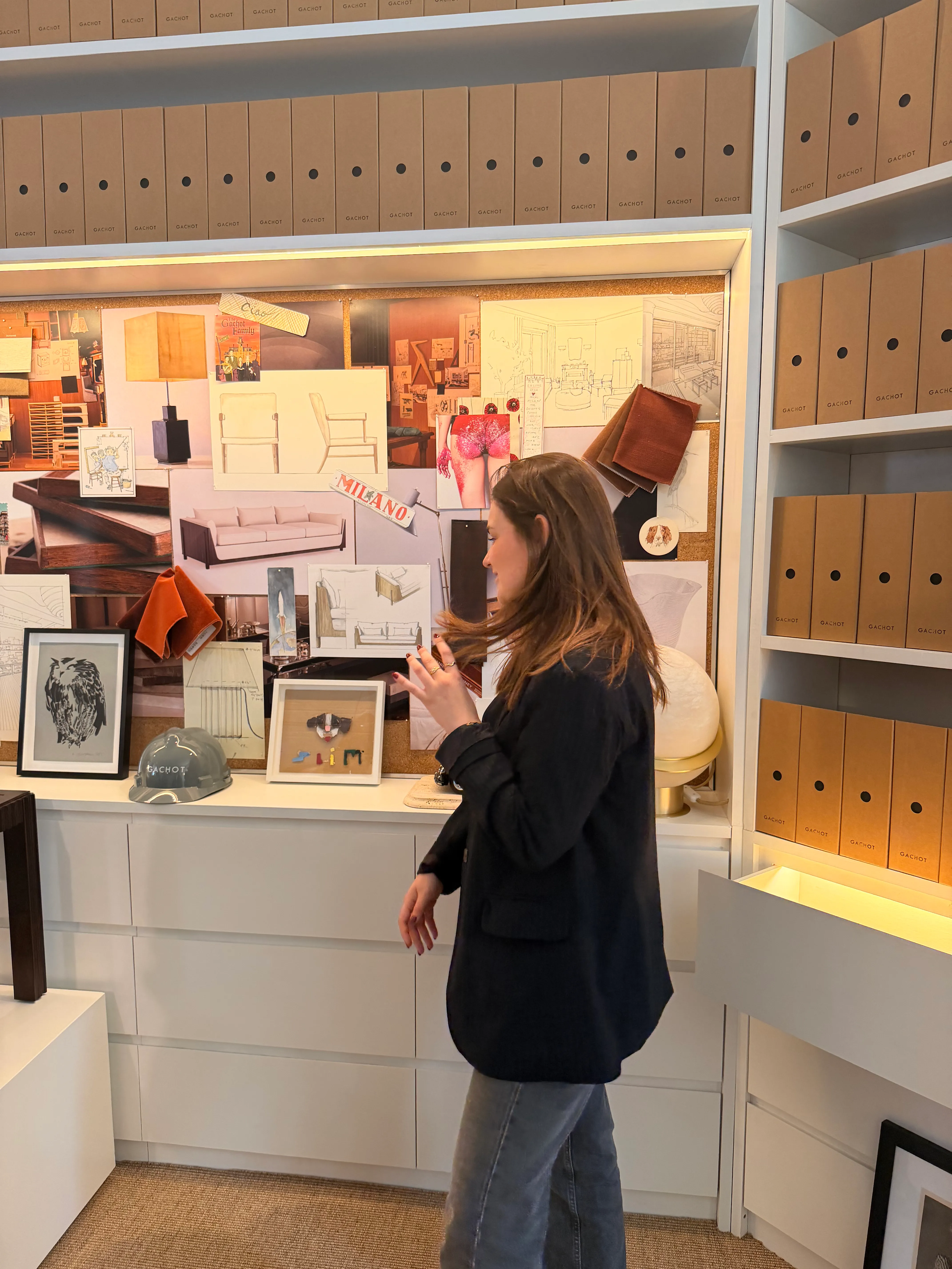 Astrid Buyse devant un moodboard de projet : croquis de mobilier, échantillons de tissus et références d'ambiance